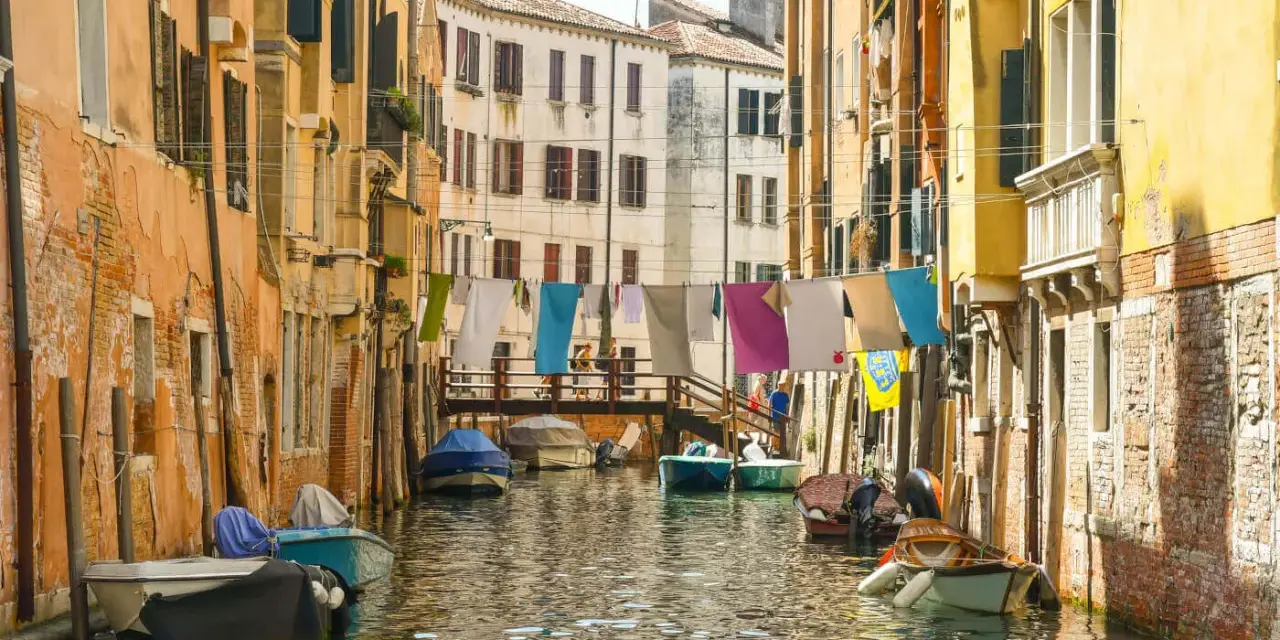 Angoli nascosti di Venezia: un canale tranquillo con barche ormeggiate e panni stesi ad asciugare tra case colorate.