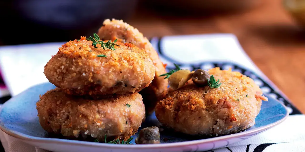 Polpette tonno e patate dorate e croccanti, guarnite con erbe aromatiche e olive, pronte per essere gustate.