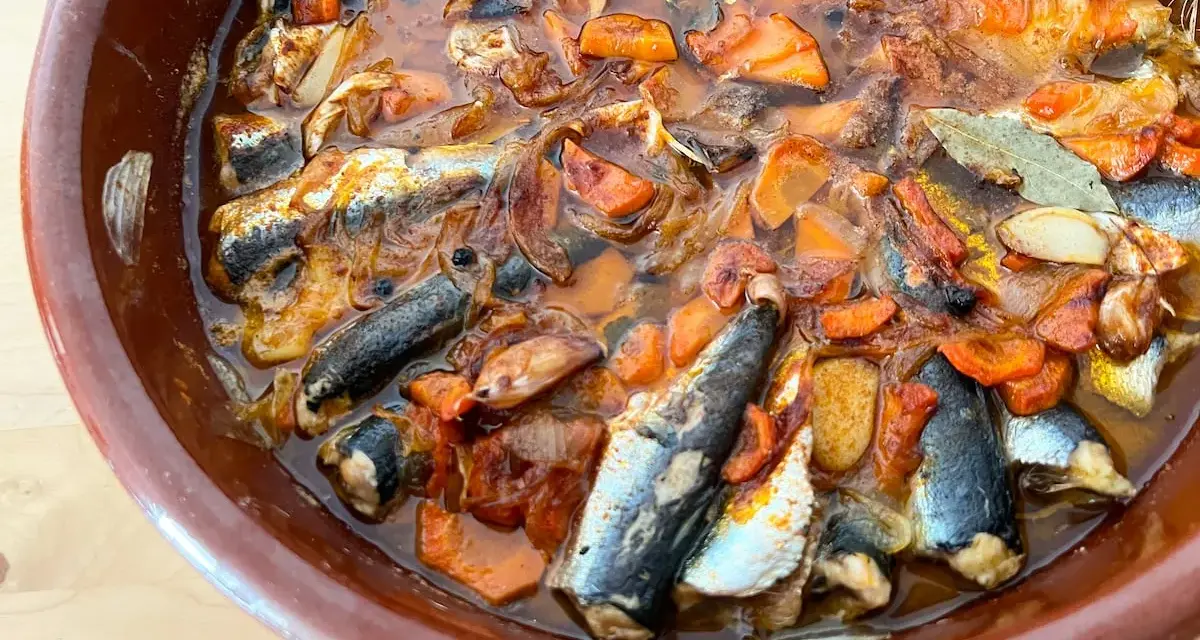 Sardinas en escabeche cocinándose en una cazuela de barro con verduras.