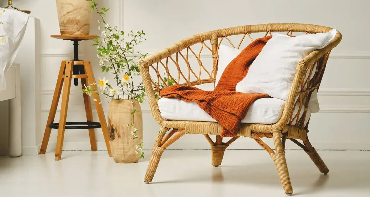 Un fauteuil en rotin tressé, invitant à la détente. Un plaid orange et un coussin blanc ajoutent une touche de confort. L'entretien rotin est essentiel pour préserver sa beauté naturelle.
