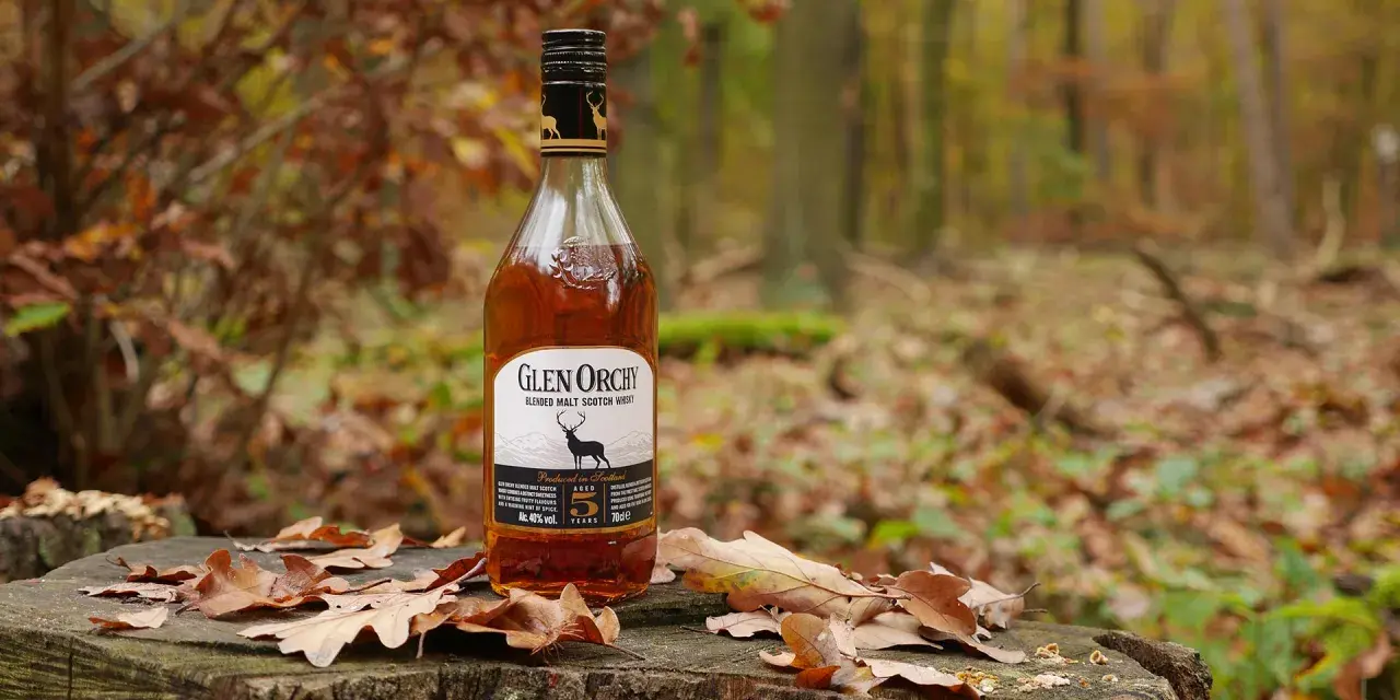 Glen Orchy Whisky steht auf einem Baumstumpf im Herbstwald, umgeben von Laub.