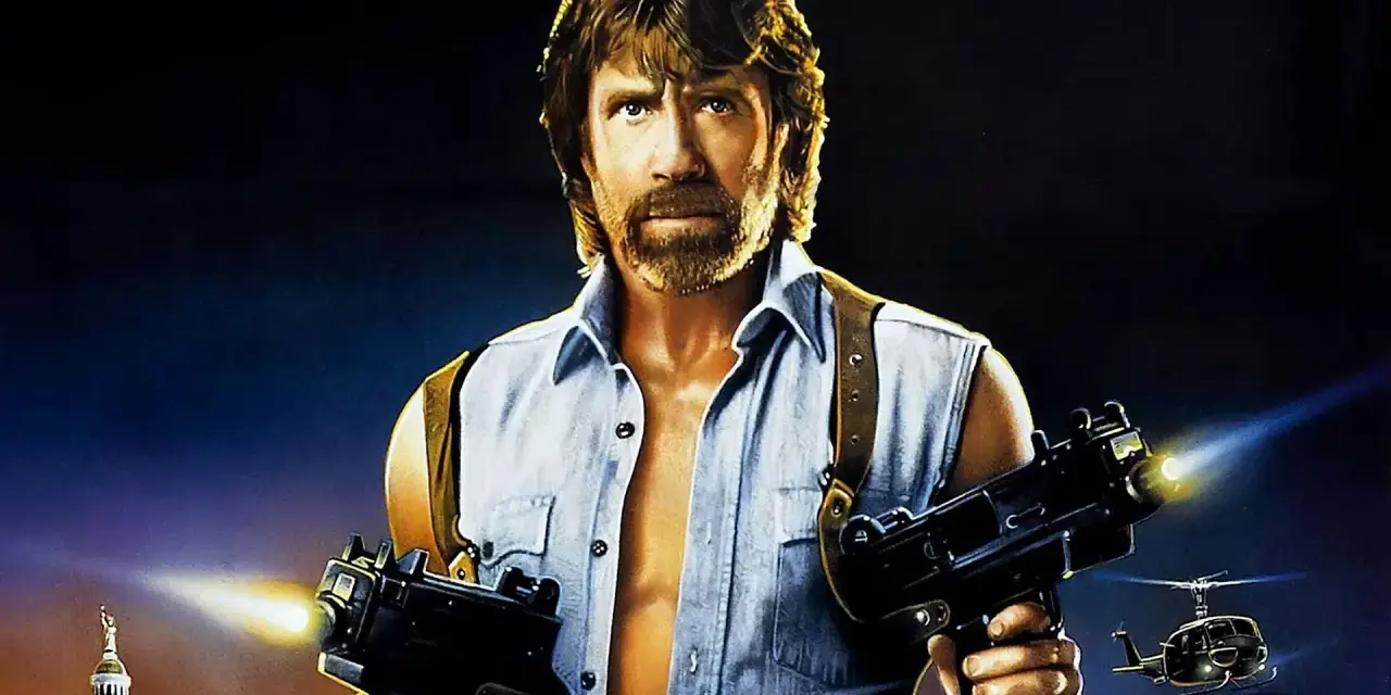 Chuck Norris z karabinami w akcji, jak w jego najlepszych filmach. W tle helikoptery i budynek.
