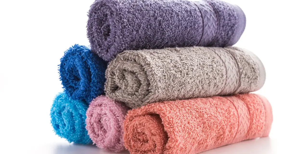 Pile de serviettes de bain roulées aux couleurs vives : violet, bleu, gris, rose et corail. La matière douce invite à la détente.