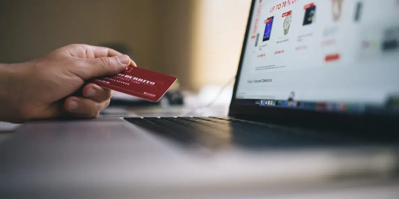 Dłoń trzyma kartę lojalnościową, przygotowując się do zakupów online. Może to być import z Wielkiej Brytanii, np. z sieci sklepów.