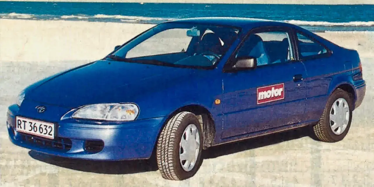 Niebieski Toyota Paseo stoi na plaży, z morzem w tle.