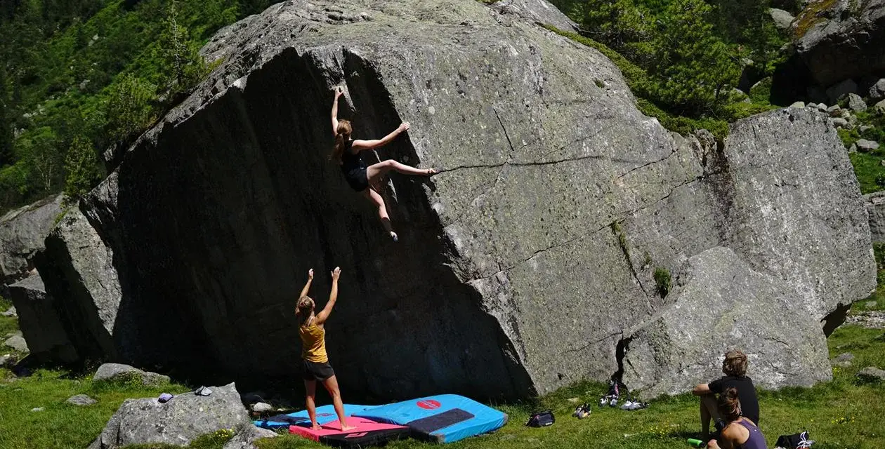 Zwei Frauen klettern an einem Felsen, eine oben, die andere unten. Das ist, was ist bouldern: Klettern ohne Seil an niedrigen Felsen.