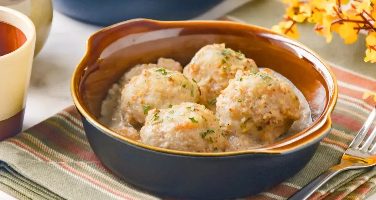 Cuatro albóndigas de merluza caseras en una cremosa salsa, espolvoreadas con perejil fresco.