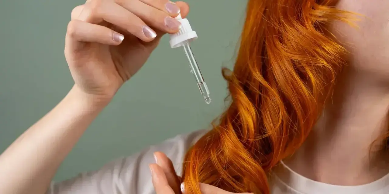 Dłoń z pipetką aplikuje olejek na rude włosy. Zastanawiasz się, ile trzymać olej na włosach?