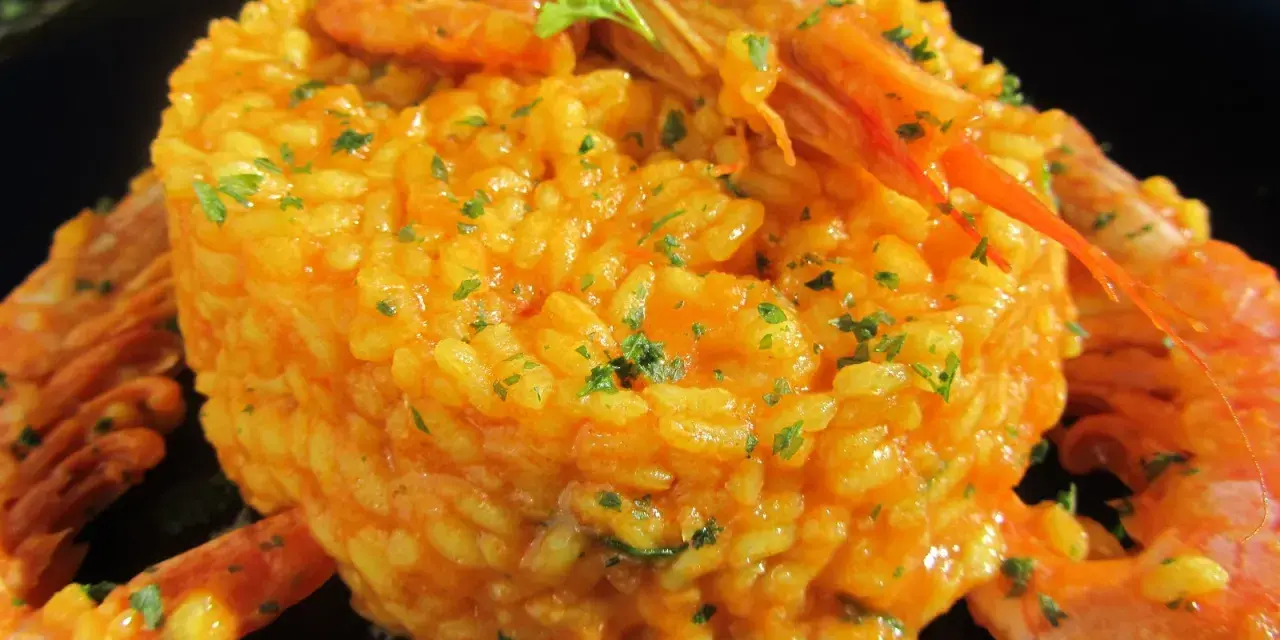 Arroz con gambones, un plato vibrante y delicioso, coronado con gambones jugosos y perejil fresco.