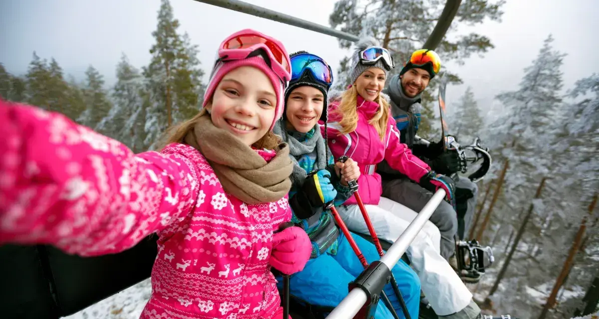 Rodzina na wyciągu narciarskim, robiąca selfie. Dziewczynka z przodu uśmiecha się szeroko. To ich wymarzone wczasy pod gruszą, ale zimowe!