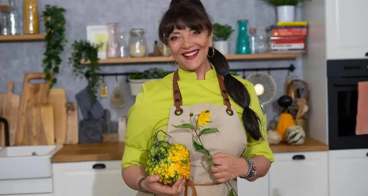 Cristina Catese w kuchni, trzymająca ozdobną dynię i słonecznik.