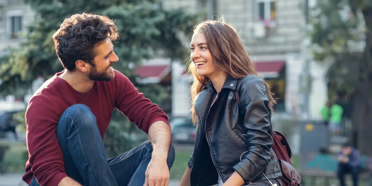 Un couple rit en s'asseyant dehors. Un moment complice pour montrer à son partenaire qu'on a envie de lui.