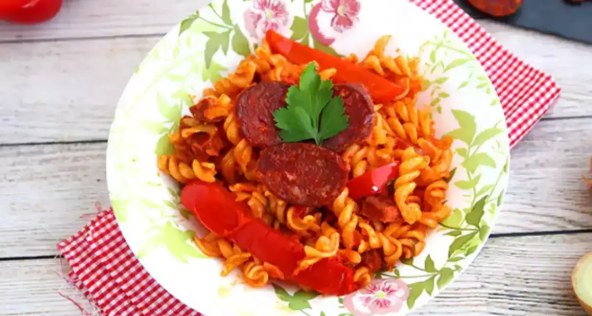 Pyszny makaron z chorizo, papryką i natką pietruszki na talerzu z motywem kwiatowym.