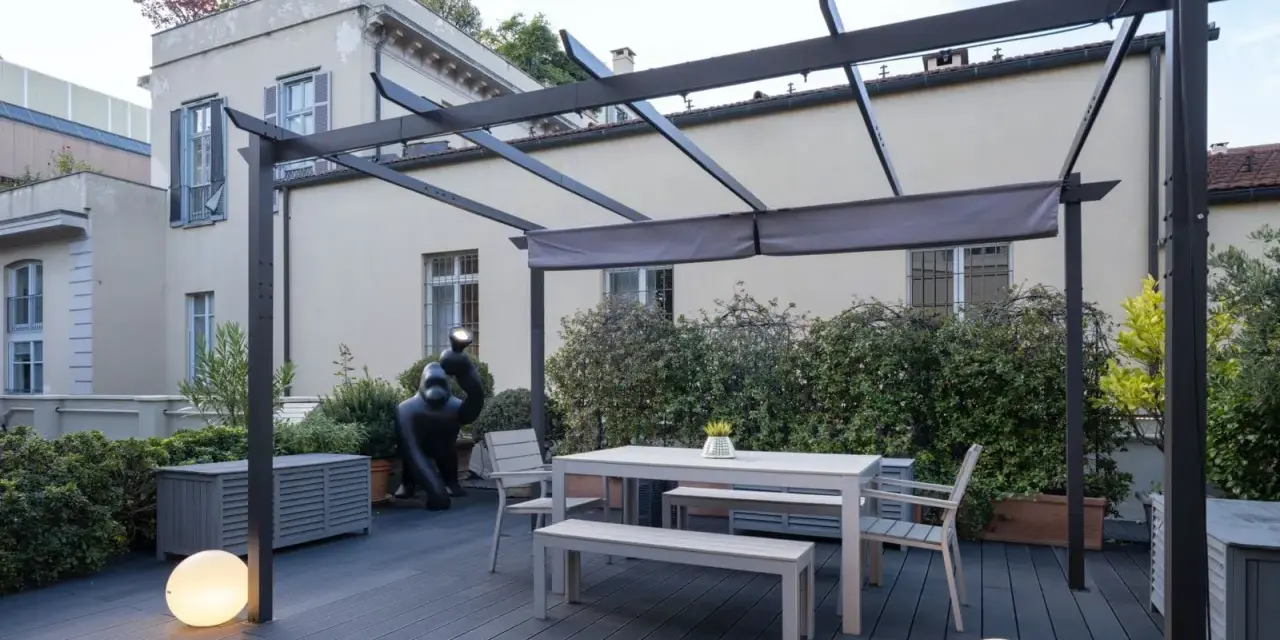 Terrazze arredate con tavolo, panche, sedie e scultura di gorilla sotto una pergola. Illuminazione soffusa con sfere luminose.