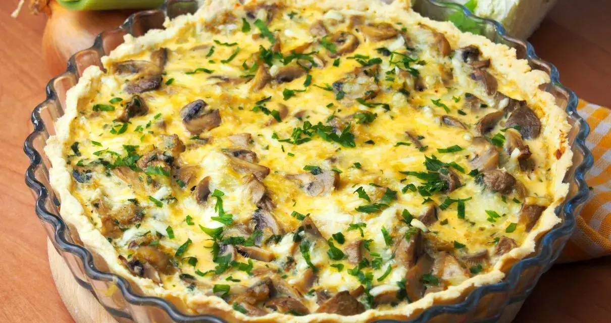 Pyszny quiche z pieczarkami, posypany świeżą natką pietruszki, w szklanej formie.