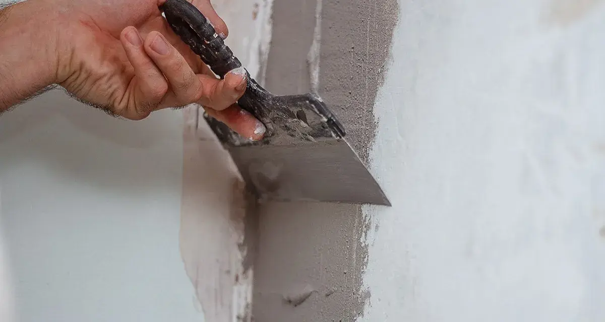 Mano che usa una spatola per stuccare un muro, creando una superficie liscia e uniforme per la pittura.