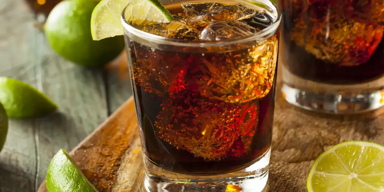 Orzeźwiający Cuba Libre, czyli rum z colą i limonką, z kostkami lodu i świeżymi ćwiartkami cytrusów na drewnianym blacie.