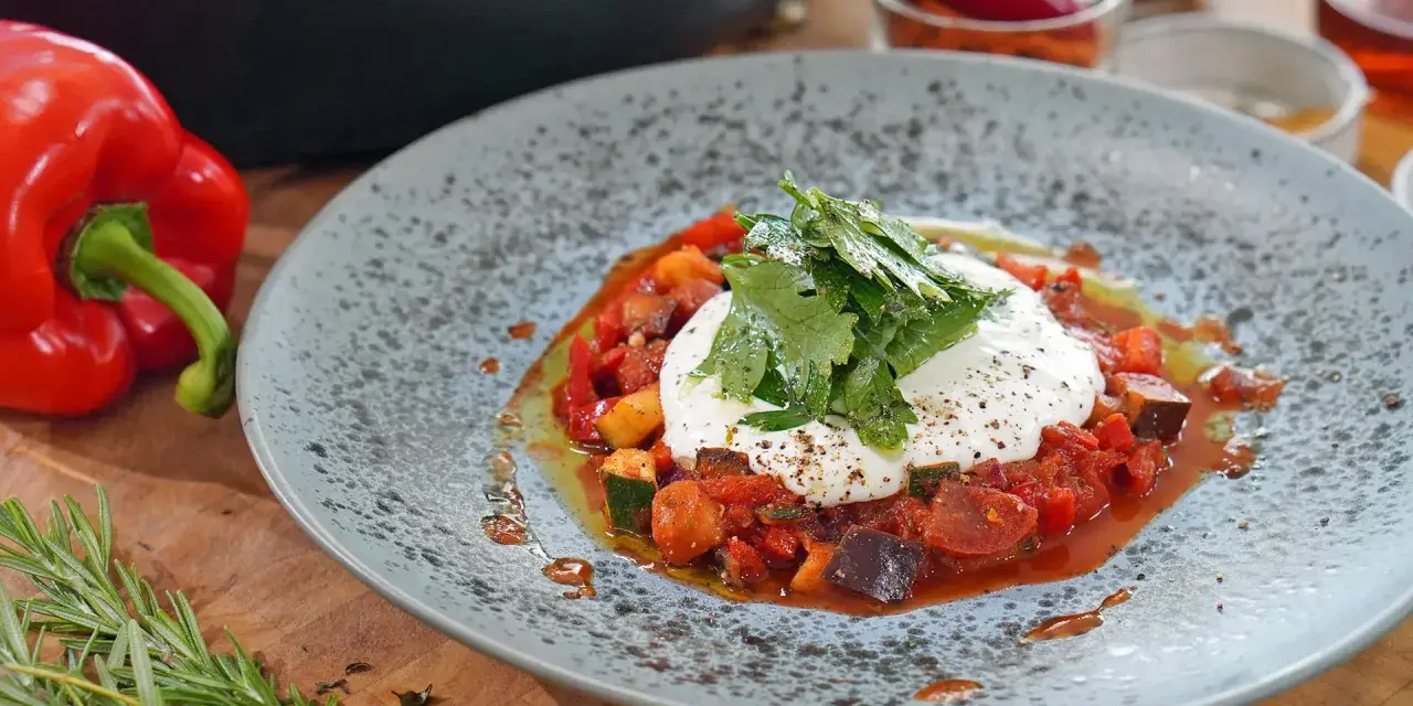 Ein Teller mit Ratatouille und Burrata, garniert mit frischen Kräutern. Dazu passt ein frischer Salat.