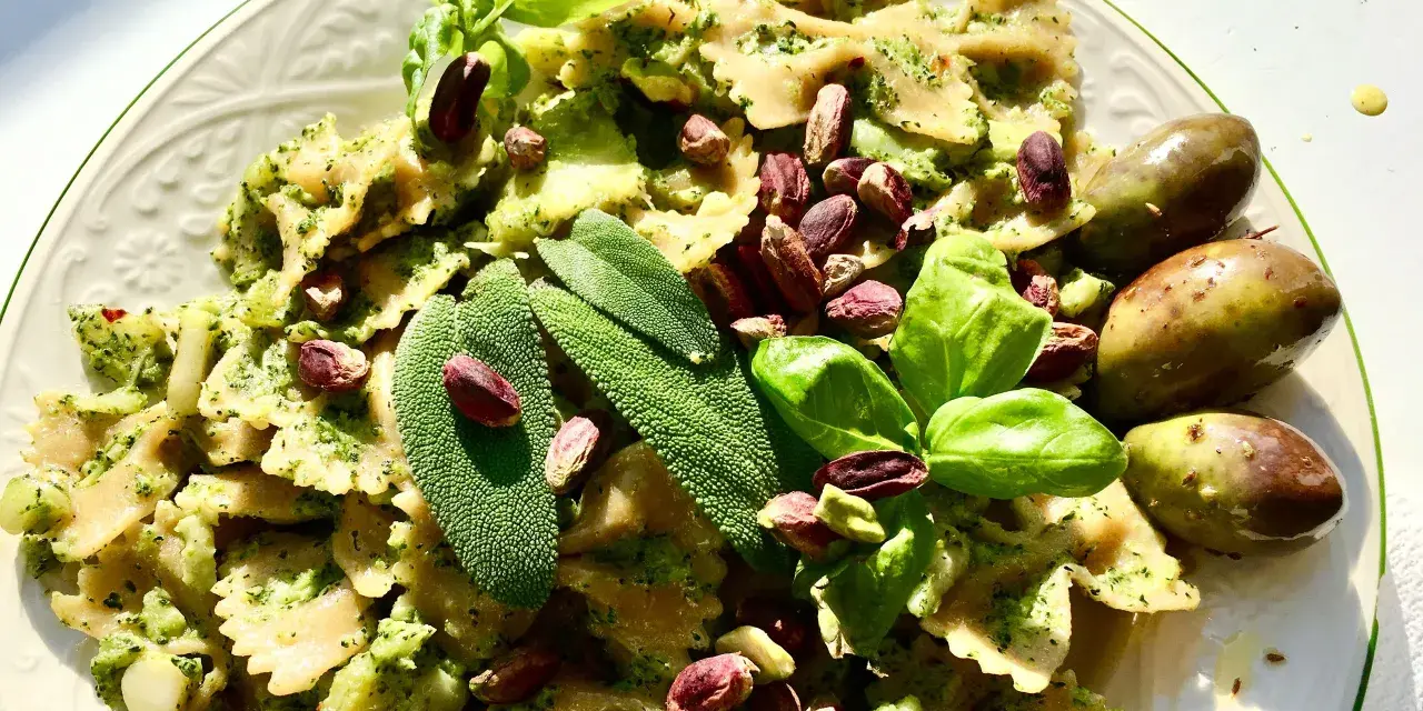 Farfalle condite con un saporito pesto di salvia, guarnite con pistacchi, basilico e olive.