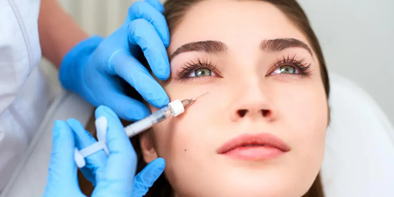 Manos enguantadas aplican inyección para tratar arrugas debajo de los ojos.