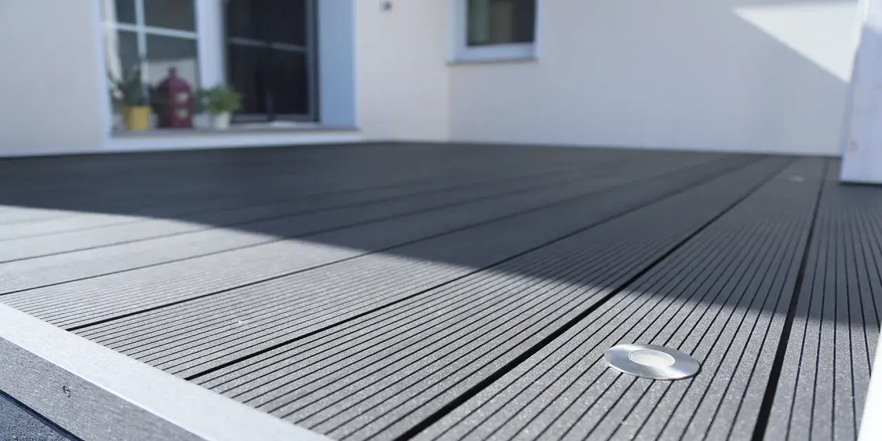 Moderne Terrasse mit grauen WPC Terrassendielen verlegen. Ein kleiner Bodenspot ist integriert.