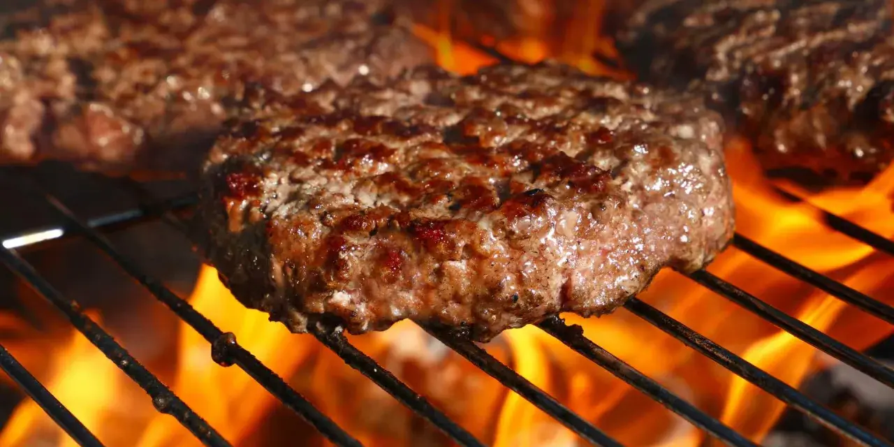 Soczyste kotlety wołowe smażące się na grillu z płomieniami.