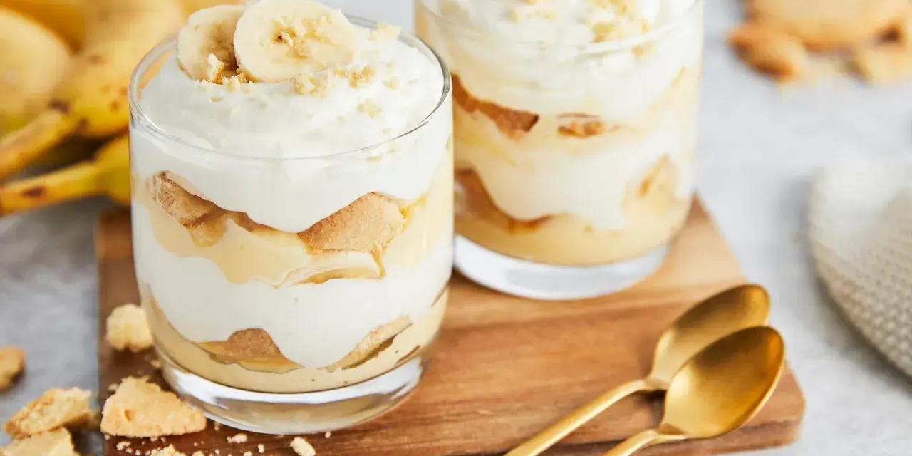 Zwei Gläser mit cremigem Bananenpudding, geschichtet mit Keksen und Bananenscheiben. Ein köstliches Bananenpudding Rezept zum Nachmachen.