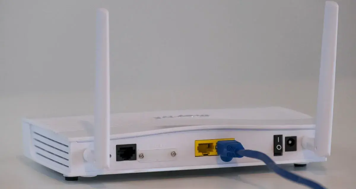 Biały modem z dwiema antenkami, podłączony niebieskim kablem Ethernet. To urządzenie, które pozwala na połączenie z internetem.