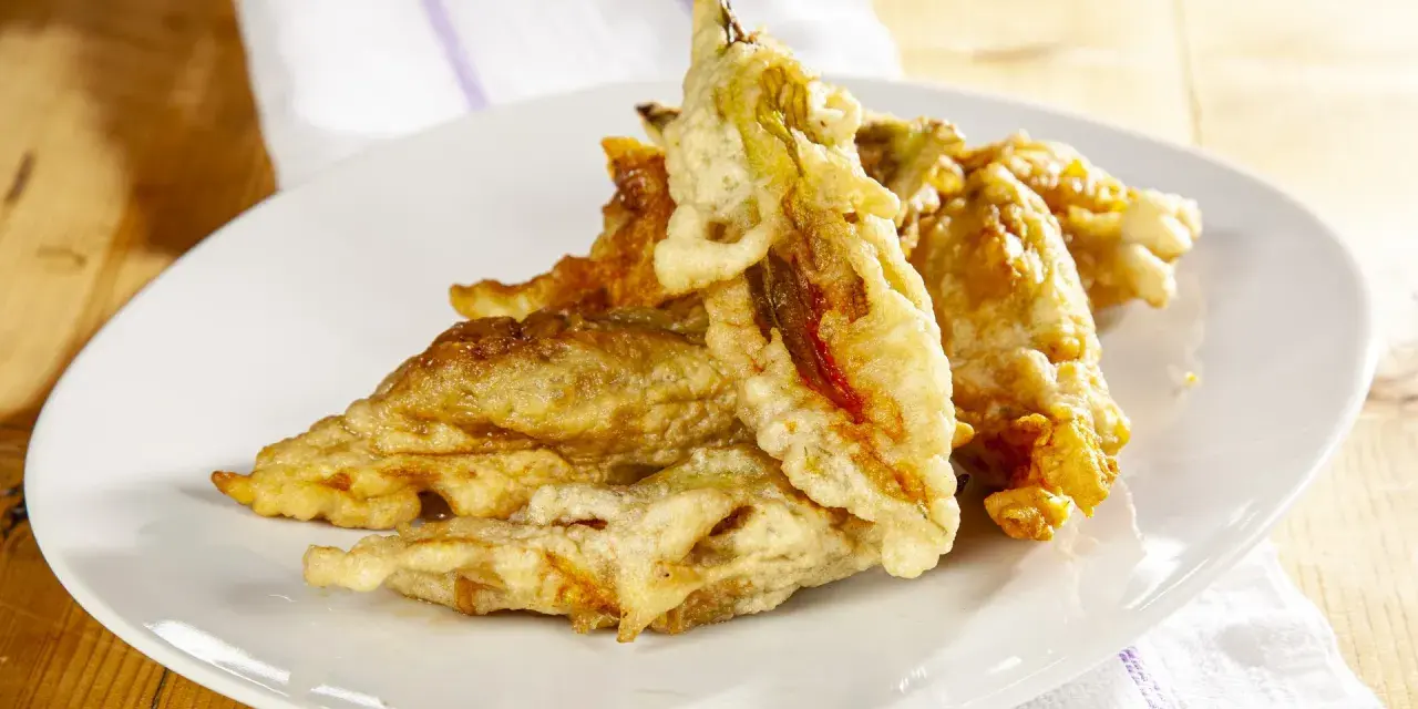Fiori di zucca fritti dorati e croccanti su un piatto bianco, pronti per essere gustati.