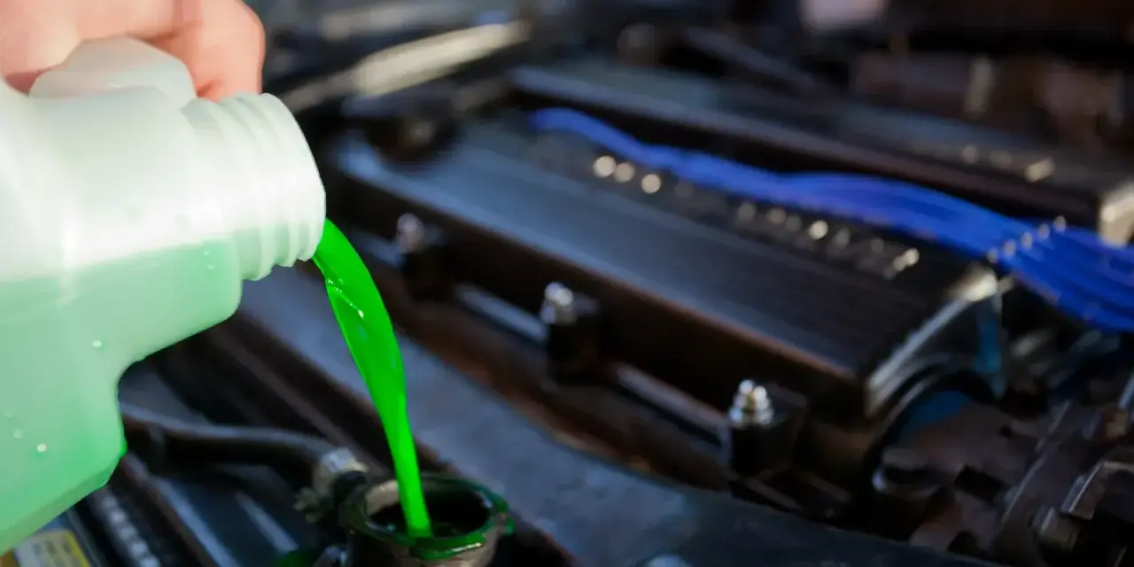 A hand pours bright green coolant into a car's radiator. This prevents the engine from overheating, unlike if coolant were mixed with oil.