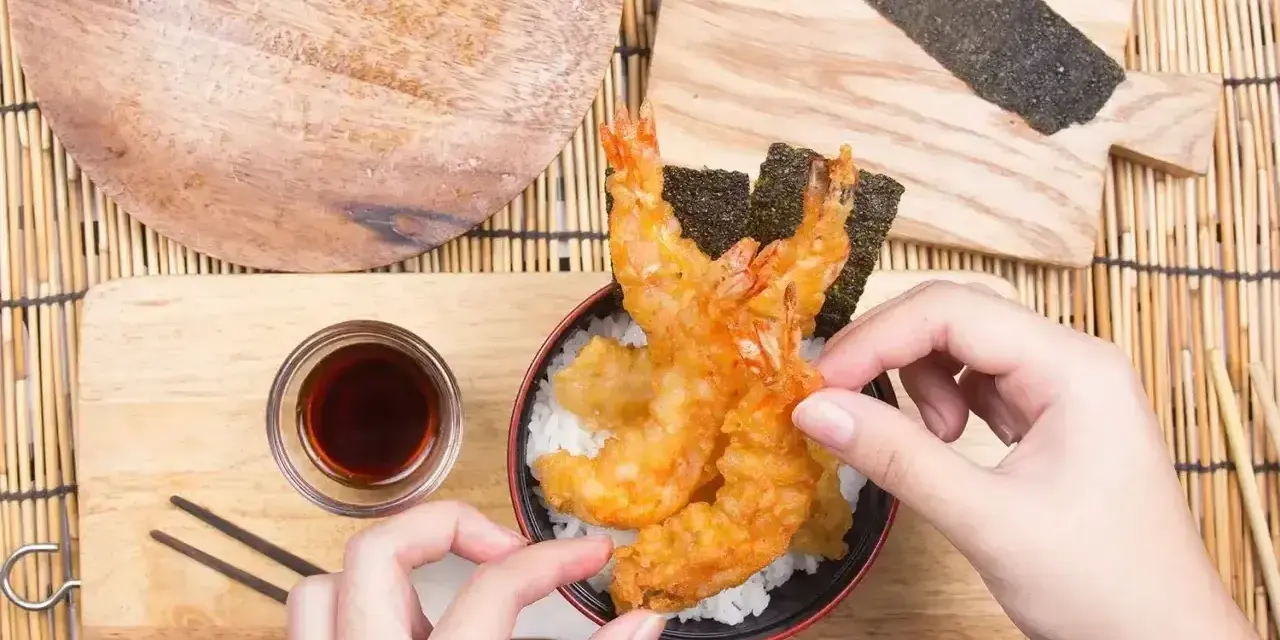 Ręce układają chrupiące krewetki tempura na ryżu. Idealny przepis na tempurę do domowego obiadu.