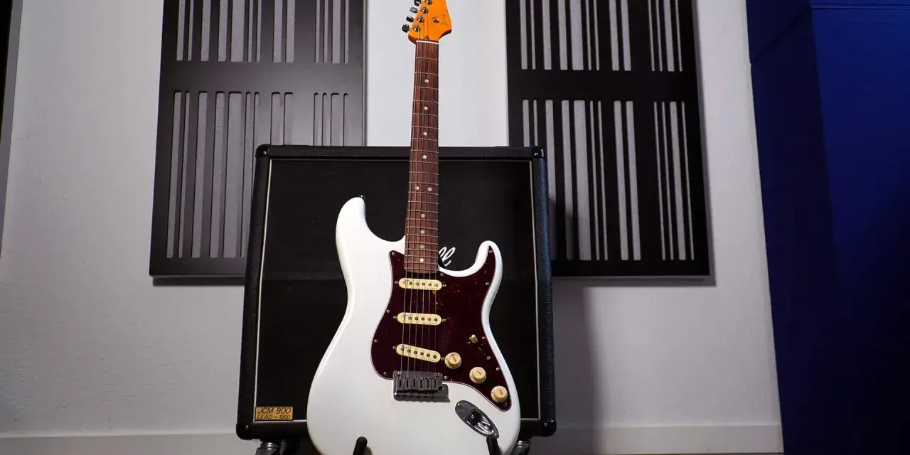 Weiße E-Gitarre mit sechs Saiten steht vor einem Verstärker.