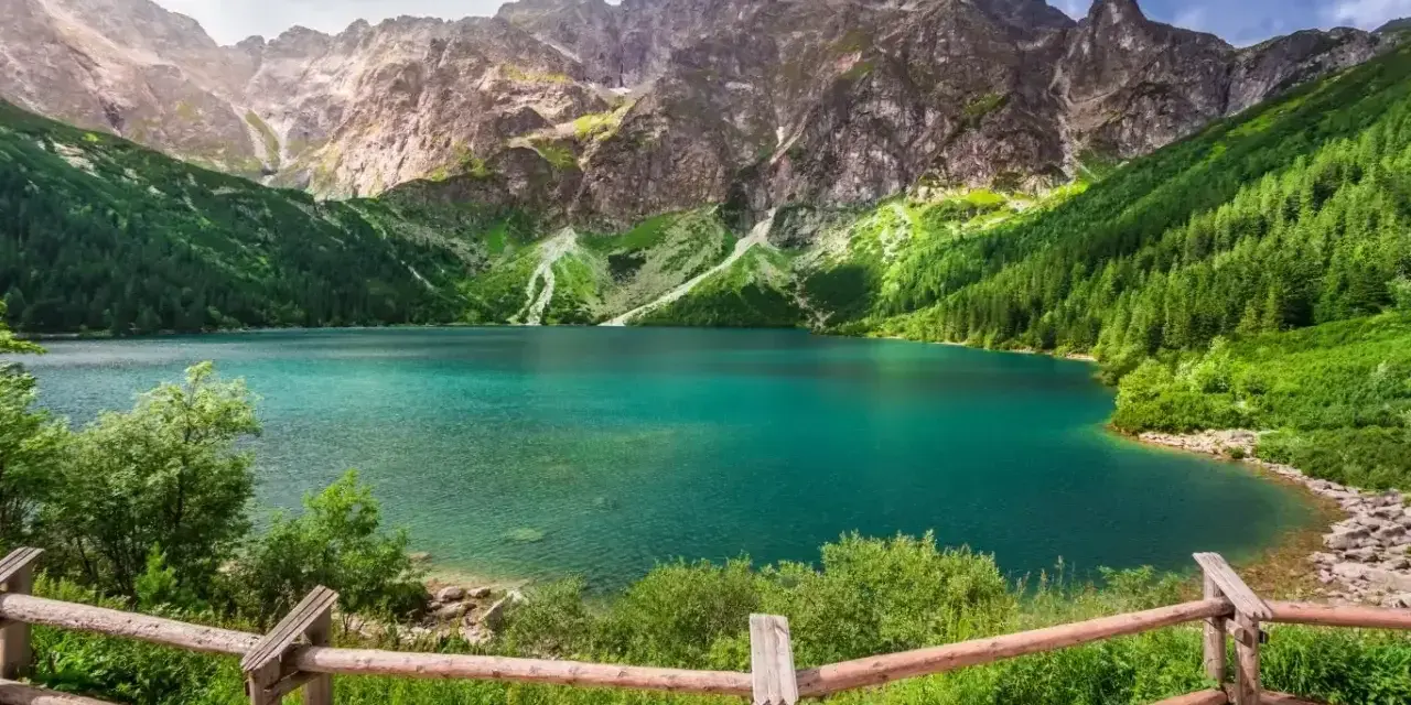 Turkusowe jezioro otoczone zielonymi zboczami gór, przypominające beskidzkie Morskie Oko.