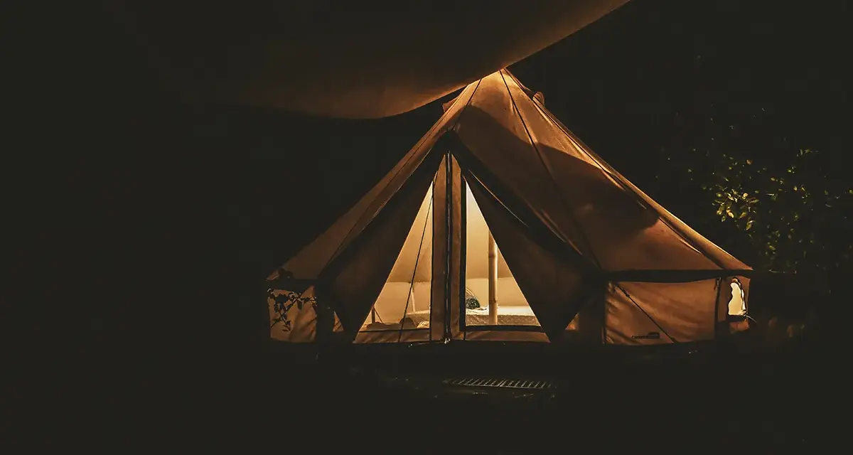 Nocą oświetlony namiot na darmowych miejscach biwakowych. Ciepłe światło wydobywa się z wnętrza, tworząc przytulną atmosferę.