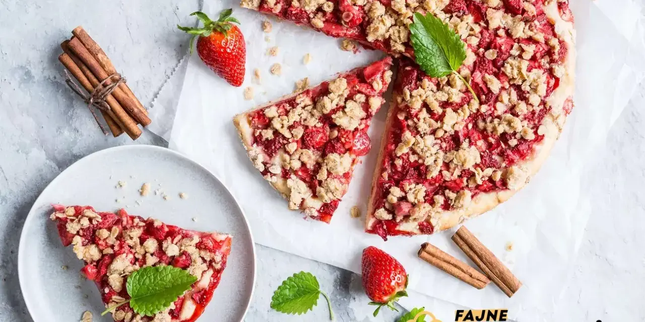 Pyszna tarta z truskawkami i kruszonką, udekorowana miętą, obok laski cynamonu i świeżych truskawek.