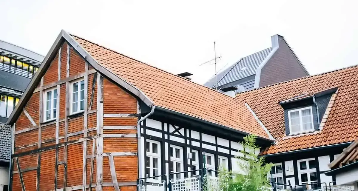 Tradycyjna **konstrukcja muru pruskiego** z ceglanymi wypełnieniami i drewnianymi belkami, obok nowoczesnych budynków.