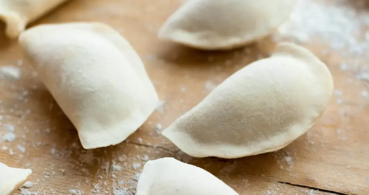 Surowe pierogi na drewnianej desce, przygotowane z ciasta na pierogi bez jajka.
