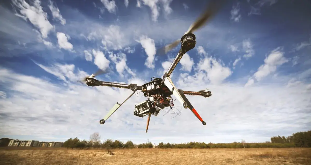 A drone hovers in a blue, cloudy sky over a dry, grassy field, hinting at the need to understand **Montana drone laws** before flying.