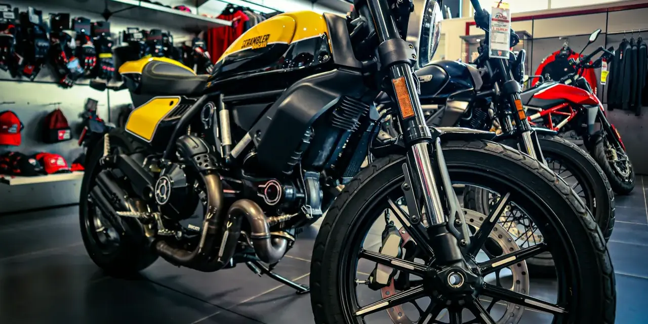 Ducati Scrambler gialla e nera, pronta per i raduni moto. Dietro, altre moto e abbigliamento tecnico.