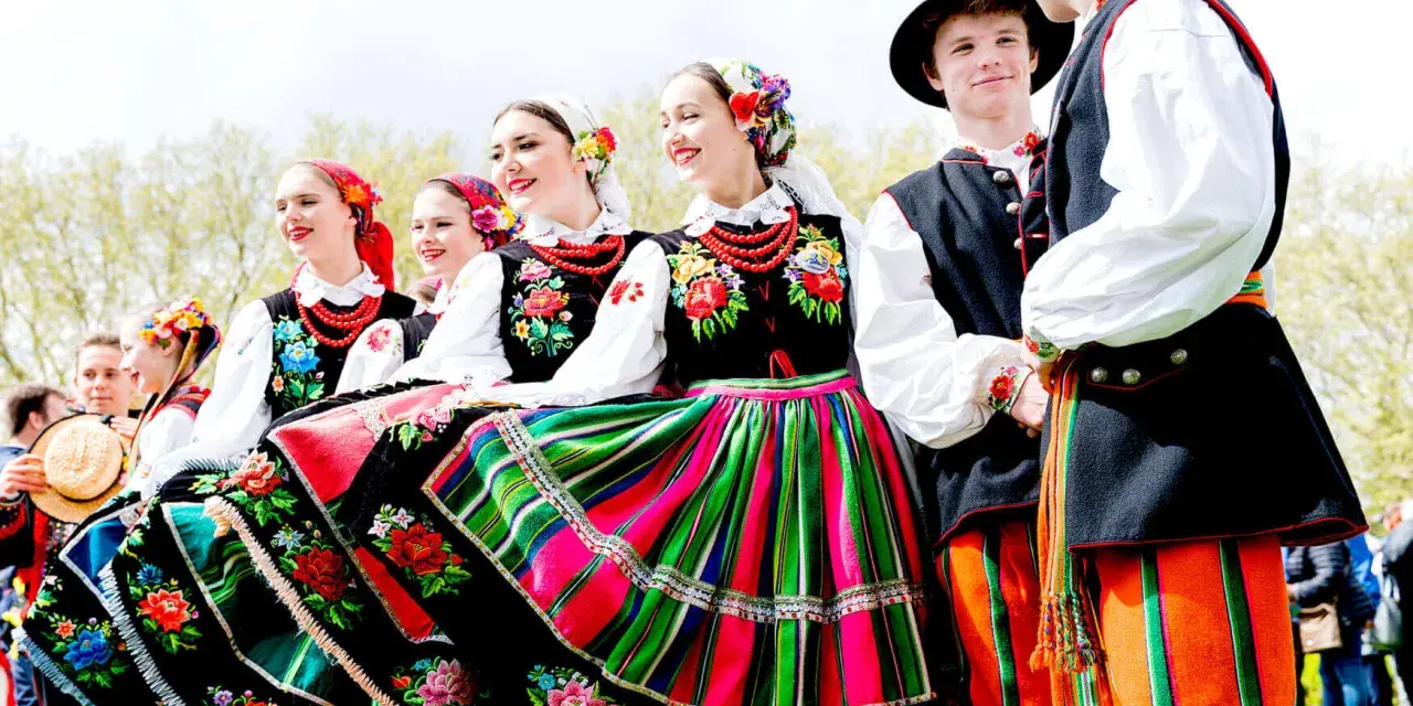 Młodzi ludzie w barwnych strojach ludowych, gotowi do wykonania polskich tańców narodowych.