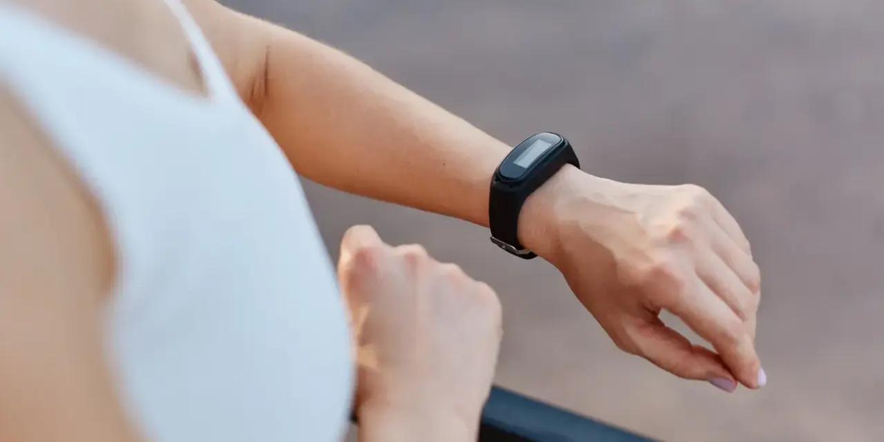 Kobieta sprawdza na swoim nadgarstku, co to jest smartband, monitorując aktywność fizyczną.