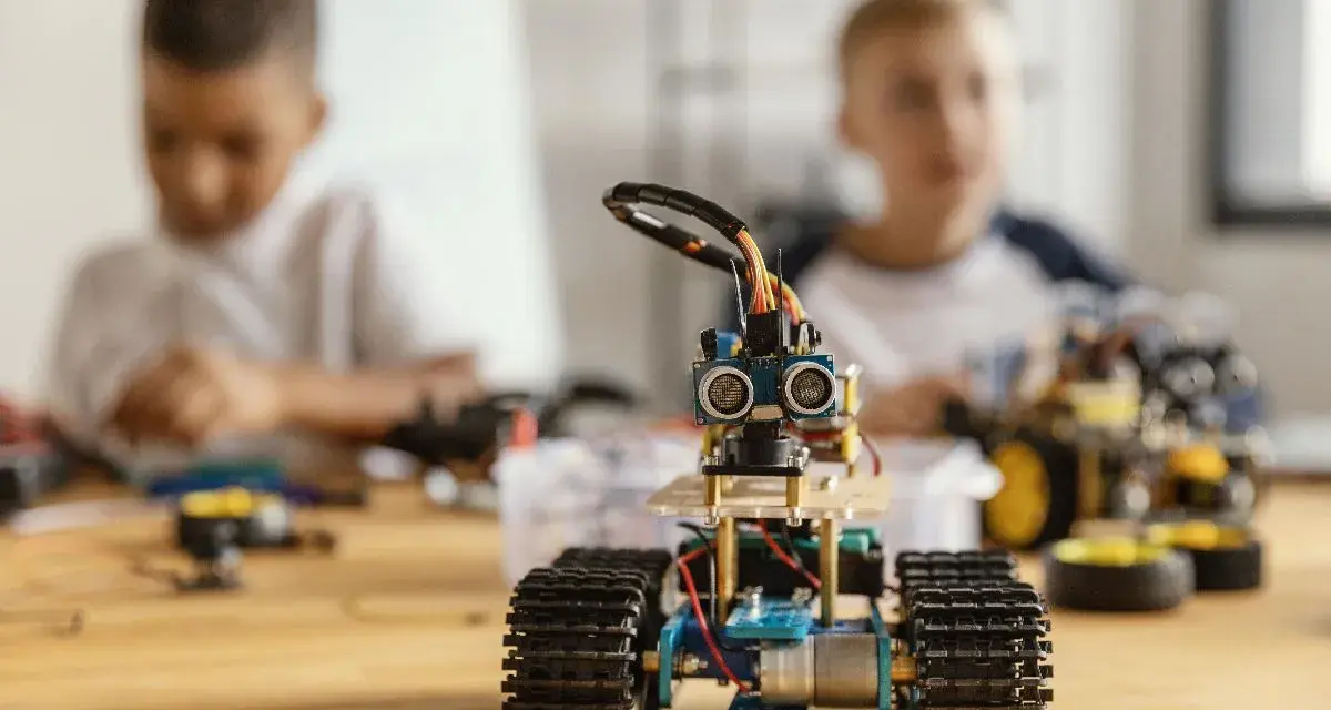 Dzieci budują roboty, ucząc się programowania i inżynierii. W centrum mały robot z czujnikami, w tle chłopcy pracujący nad projektami.