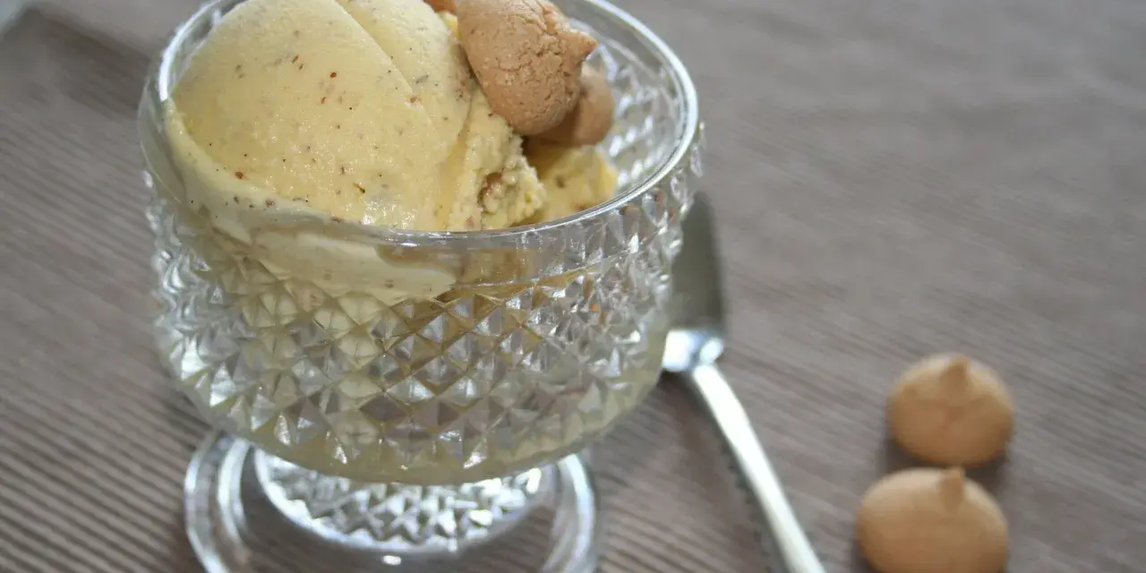 Ein Glas mit cremigem Marzipan Eis, garniert mit kleinen Keksen. Daneben liegen zwei weitere Kekse und ein Löffel.