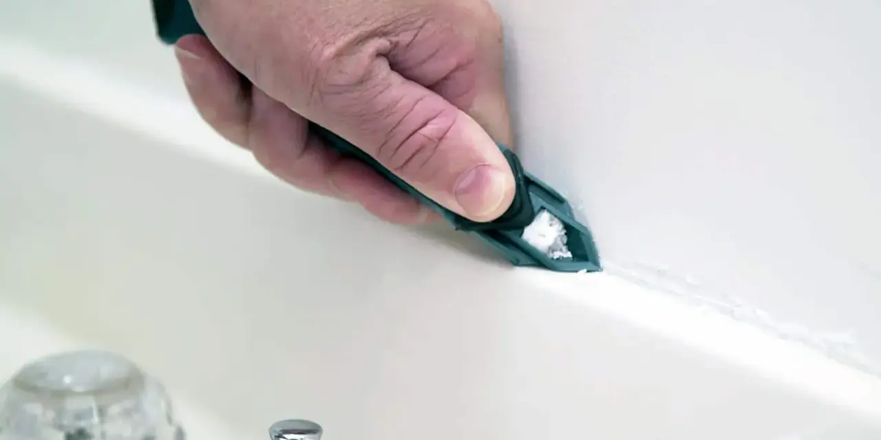 A hand uses a tool to smooth fresh caulk along a bathtub seam, demonstrating how to caulk for a clean finish.