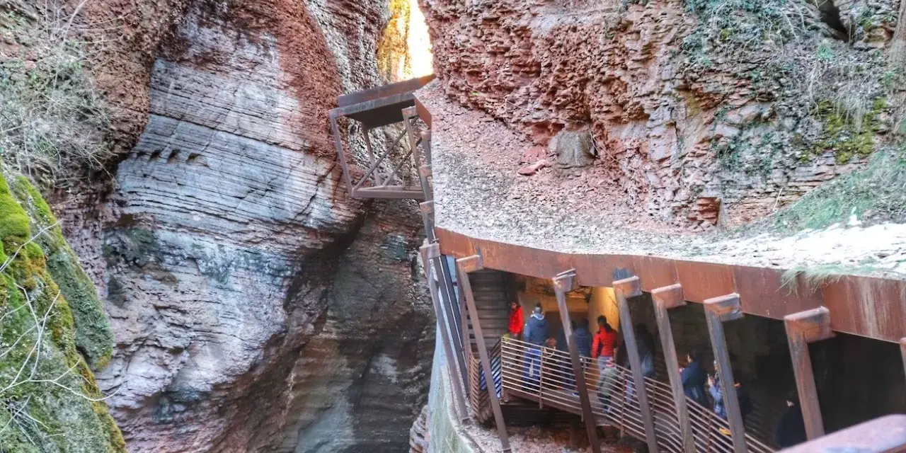 Un orrido ponte alto attraversa una gola rocciosa, con persone che salgono una scalinata metallica.