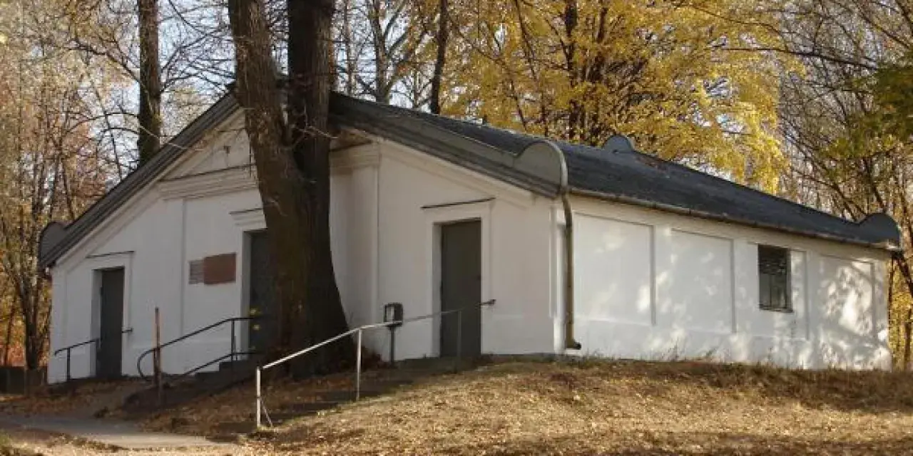 Ohel cadyka Elimelecha w Leżajsku zwiedzanie. Biały budynek z drzwiami i oknem, otoczony drzewami jesienią.