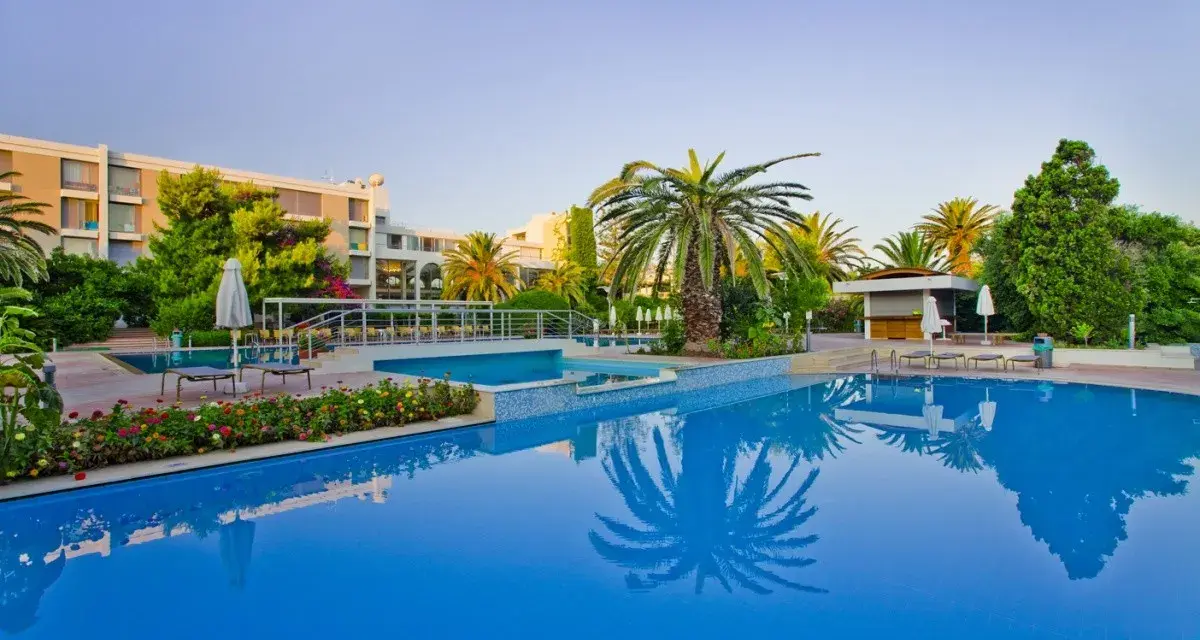 Basen hotelowy z palmami i kwitnącymi kwiatami, idealne miejsce na relaks przy Caravia Beach Kos.