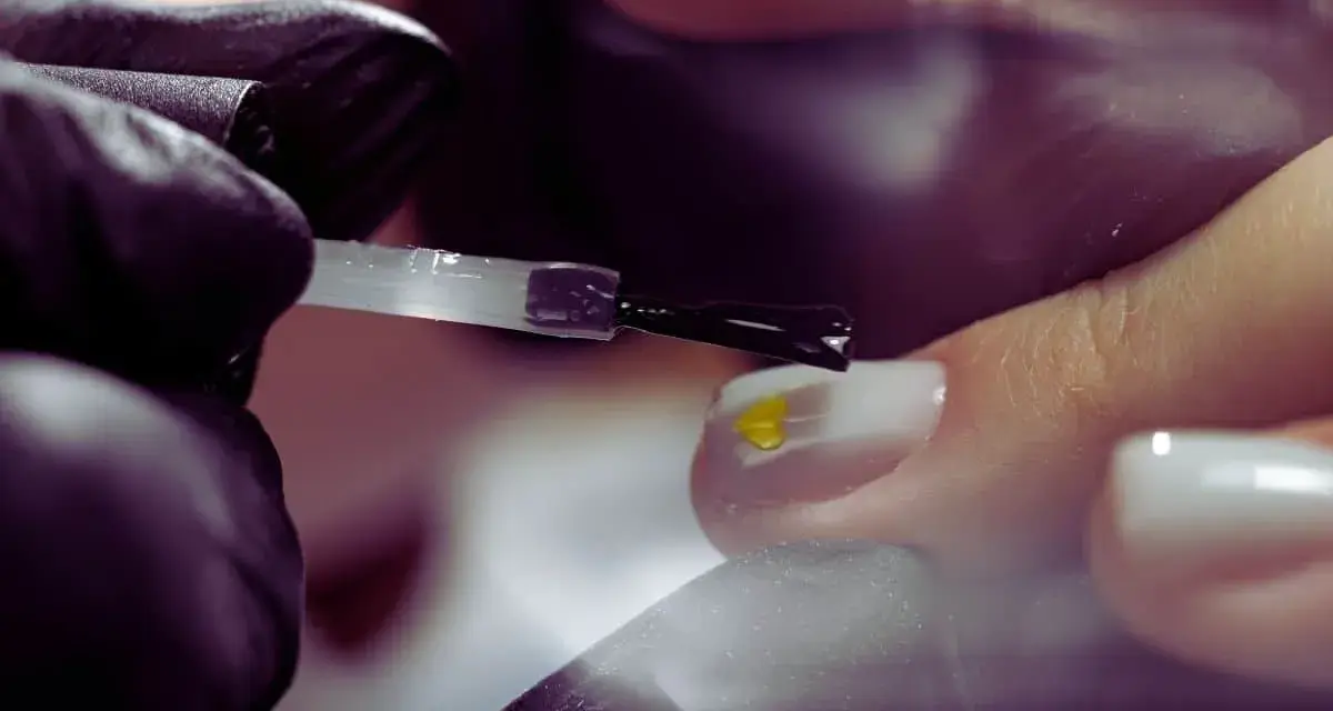 Application d'un vernis transparent sur un ongle orné d'un petit cœur jaune. Le base coat, c'est quoi ? C'est la première étape pour une manucure parfaite.