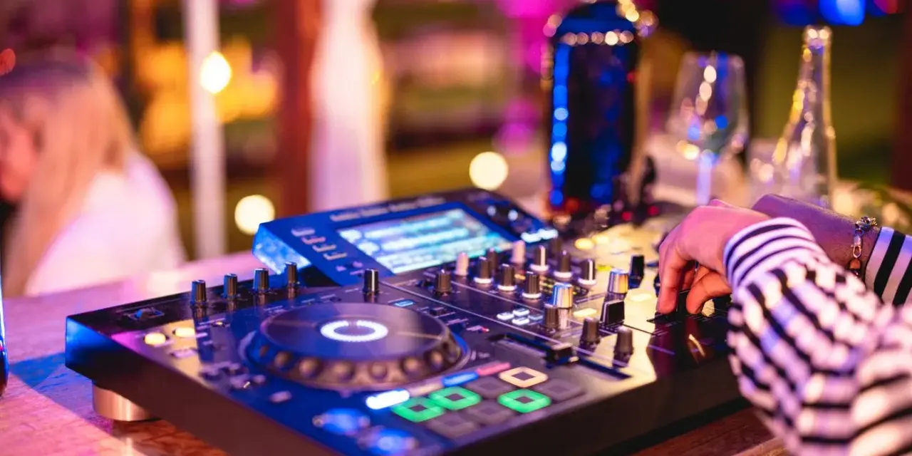 Main d'un dj house connu manipulant la console, lumières vives et ambiance festive.