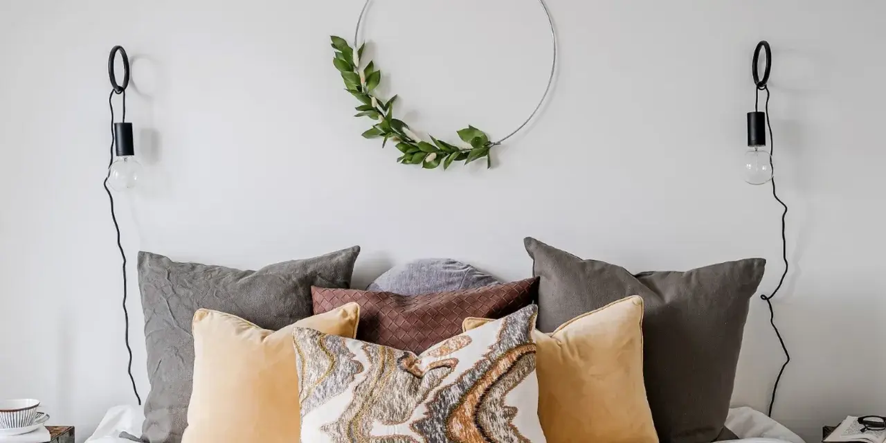Mysigt sovrum inspiration med en rund väggdekoration av gröna blad, flera kuddar i olika färger och texturer, samt svarta vägglampor.